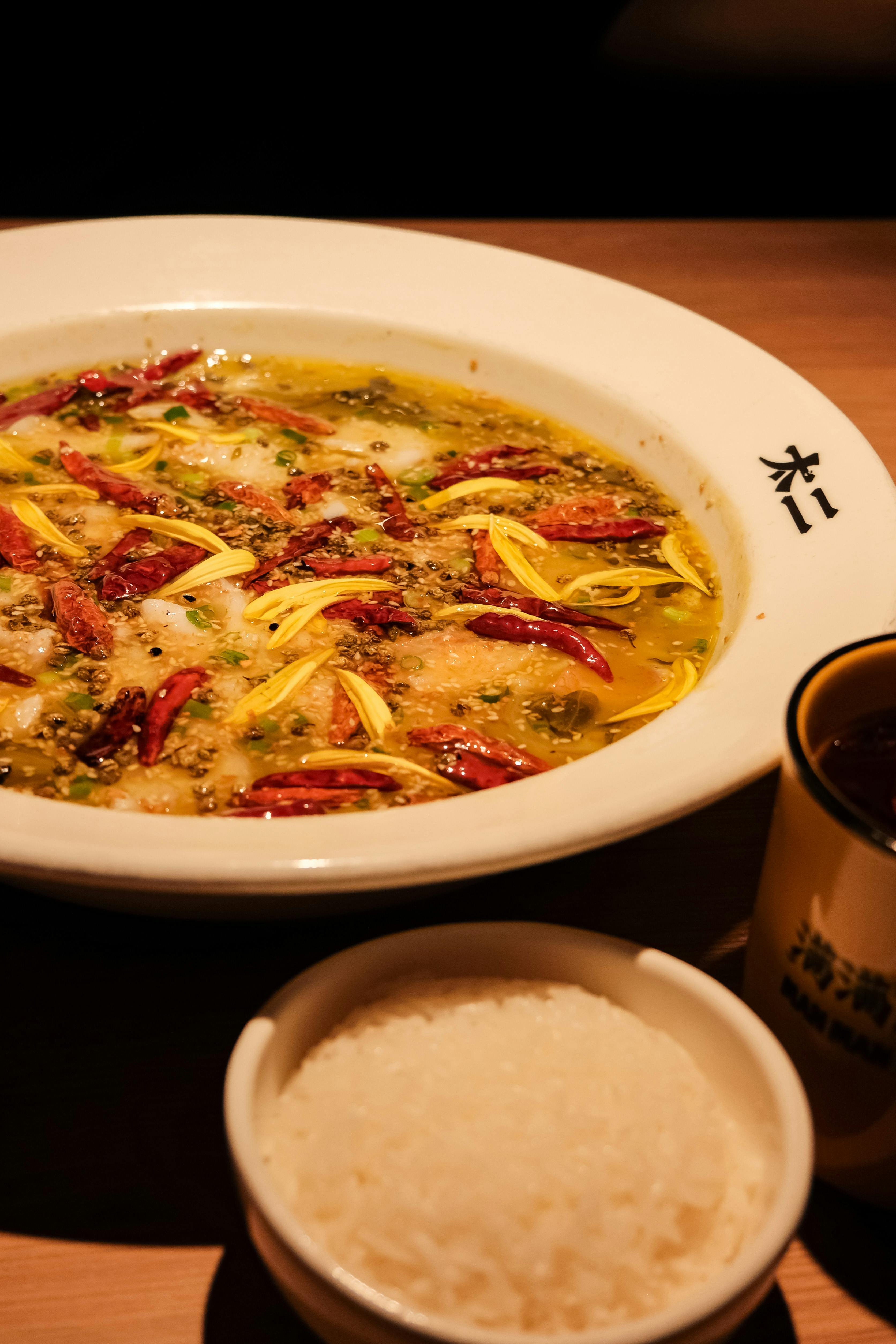 Delicious spicy Asian fish soup served with rice, featuring vibrant chili peppers and herbs.