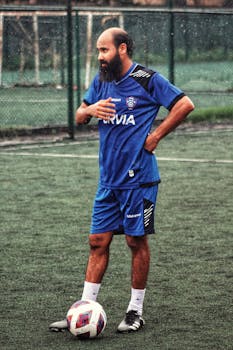 Bearded male soccer player standing on a rainy field ready for a match.