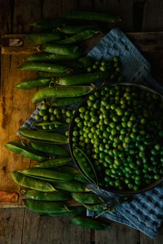 Overhead view of fresh green peas in pods on a rustic wooden table. Ideal for food and agriculture themes.