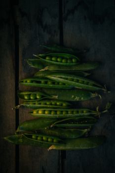 Close-up of green peas in pods arranged on a rustic wooden surface.