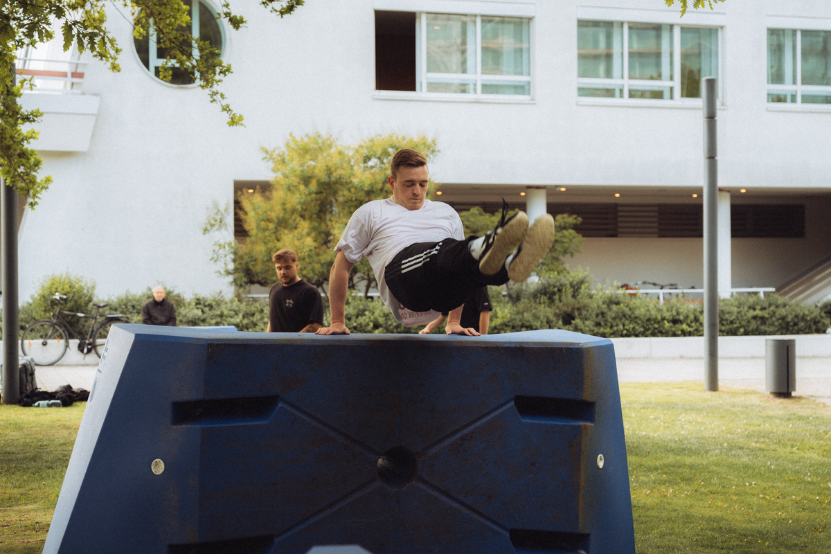 A traceur vaulting a blue parkour obstacle with both hands planted and knees tucked, the hand position a kong-style vault is built on.