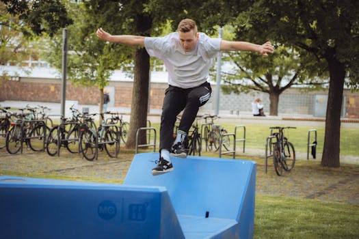 A young man jumping over blue parkour equipment in a park with bikes in the background.
