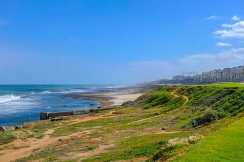 Free Beautiful coastal landscape in Rabat, Morocco with ocean waves and green hills under a clear blue sky. Stock Photo