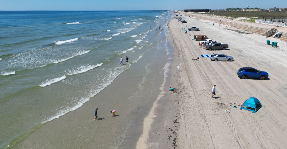 Serene aerial view of a sunny day on North Padre Island beach, Texas with cars and people enjoying the shoreline.