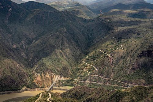 Free Scenic aerial view of a bridge crossing a river amidst the rugged terrain of the Andes mountains. Stock Photo