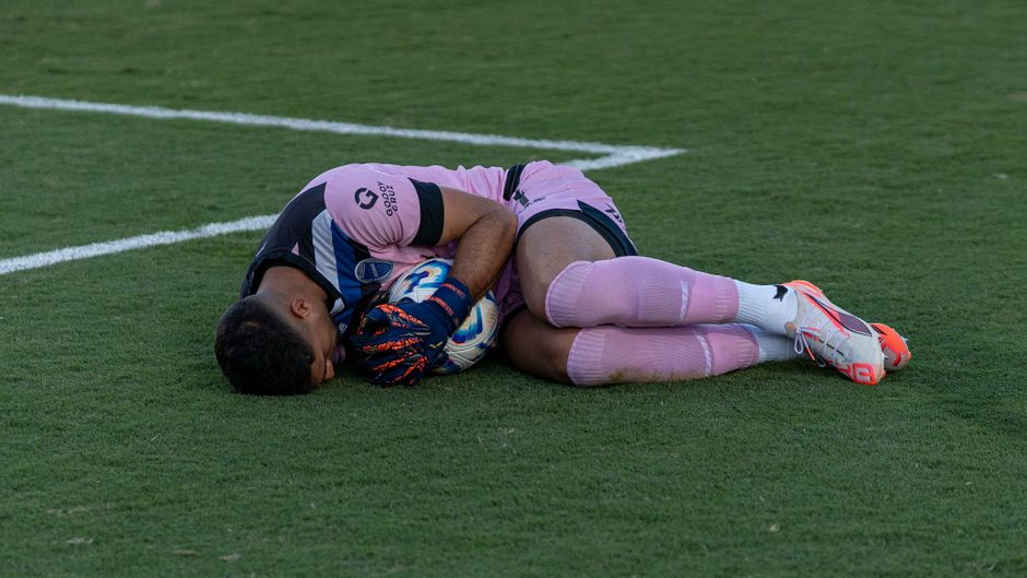 A soccer player in pink gear resting on the field, hugging a ball, possibly taking a break after a match.