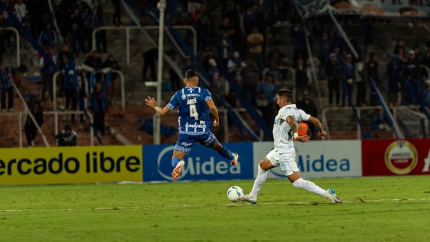 Intense football match capture with two players battling for the ball amid a cheering crowd.