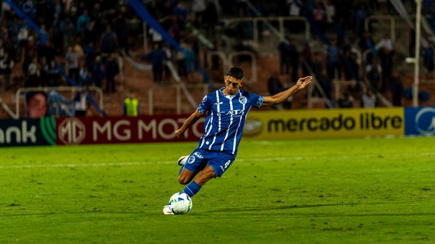 A soccer player in blue uniform kicks the ball during a match on a well-lit field.