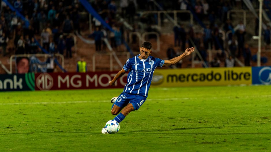 A soccer player in blue uniform kicks the ball during a match on a well-lit field.