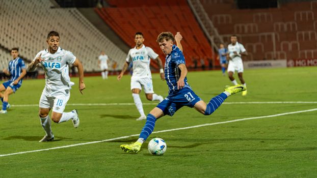 Dynamic action shot of a soccer match with players in blue and white jerseys on a green field.