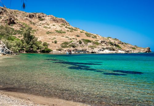 Free A picturesque beach with crystal clear waters and rocky hills under a vibrant blue sky. Stock Photo