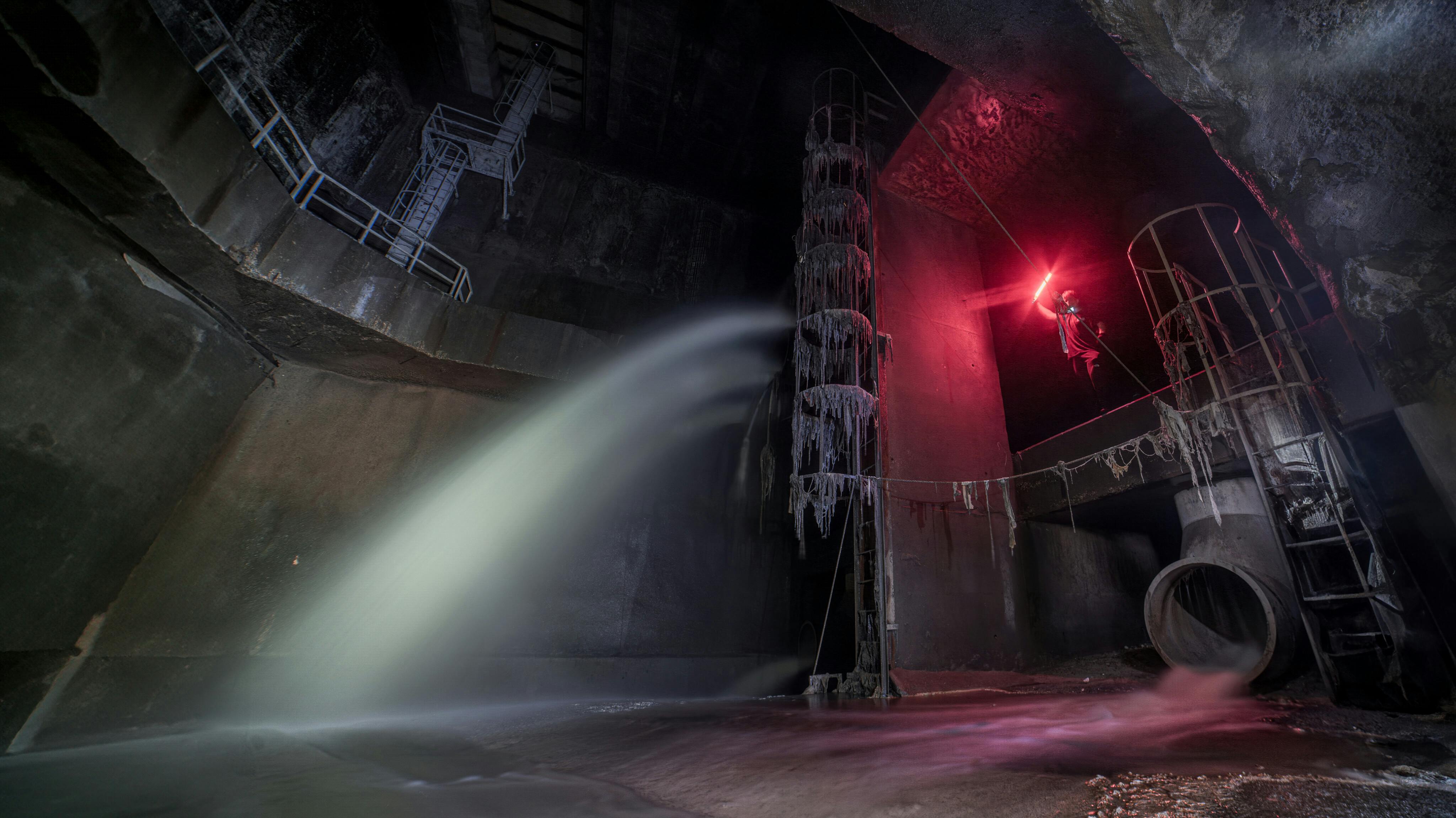 Person exploring an industrial underground with dramatic lighting and water flow.