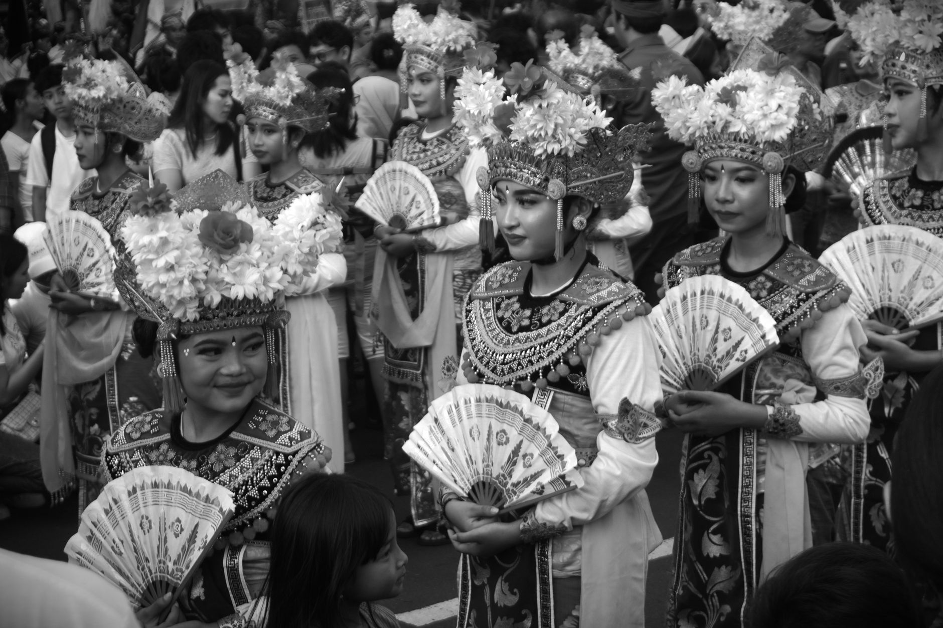 Black and white image of Balinese dancers in traditional attire at a cultural festival parade.
