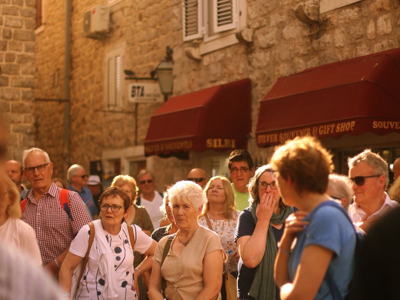 A diverse group of tourists walks through a historic city street with stone buildings - team-building history walks