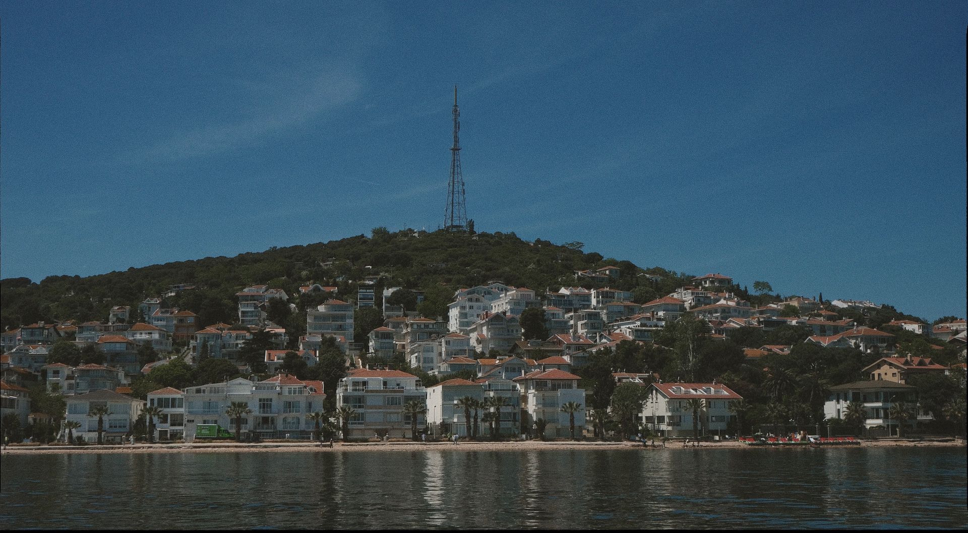 Scenic view of a hillside town by the water with a radio tower in clear blue skies.