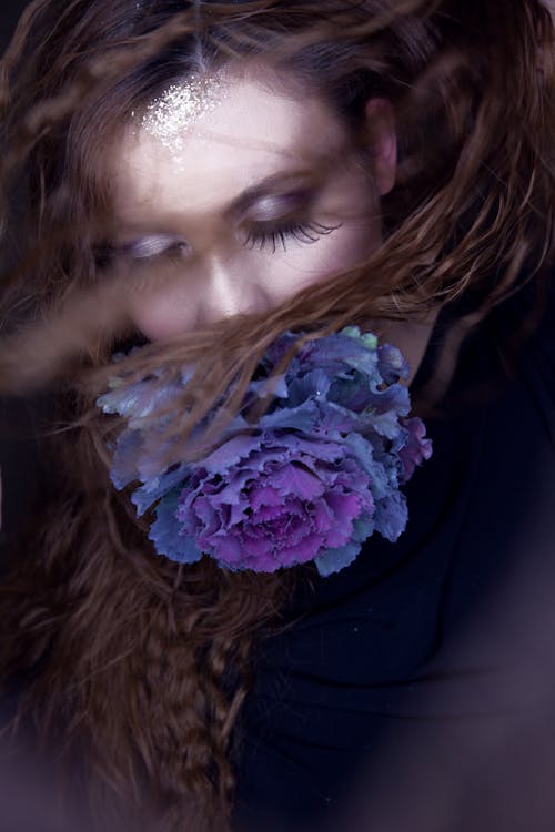 Concept Photography Of A Woman With Extra Long Lashes With A Blue Flower Covering Her Mouth