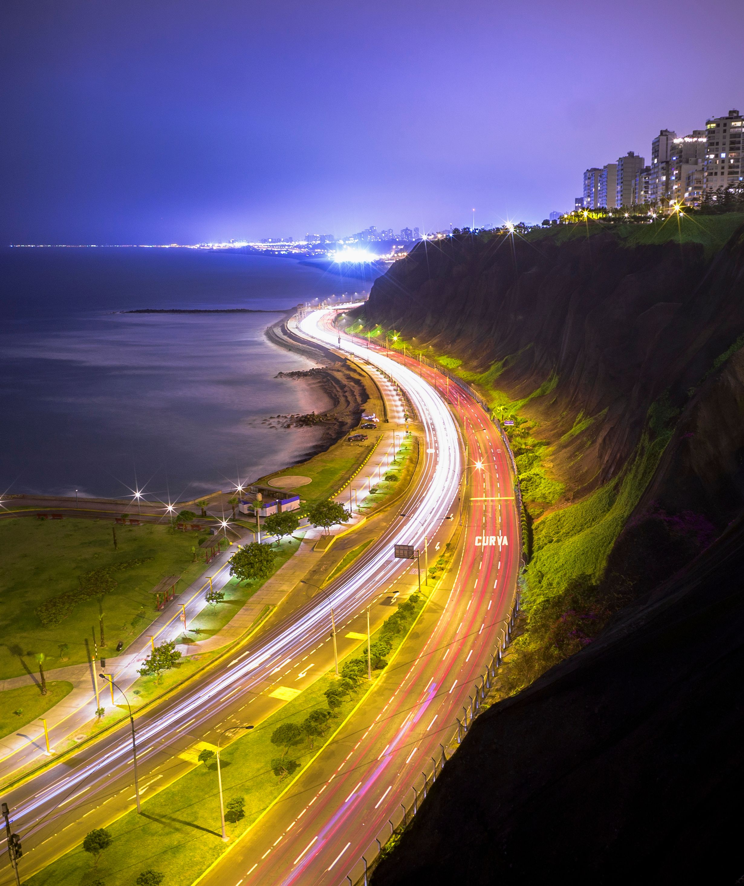 A vibrant aerial shot of Lima's coastline at night, showcasing urban lights against the ocean.