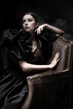 Dramatic portrait of a woman in vintage fashion, wearing a veil, seated on an ornate chair.