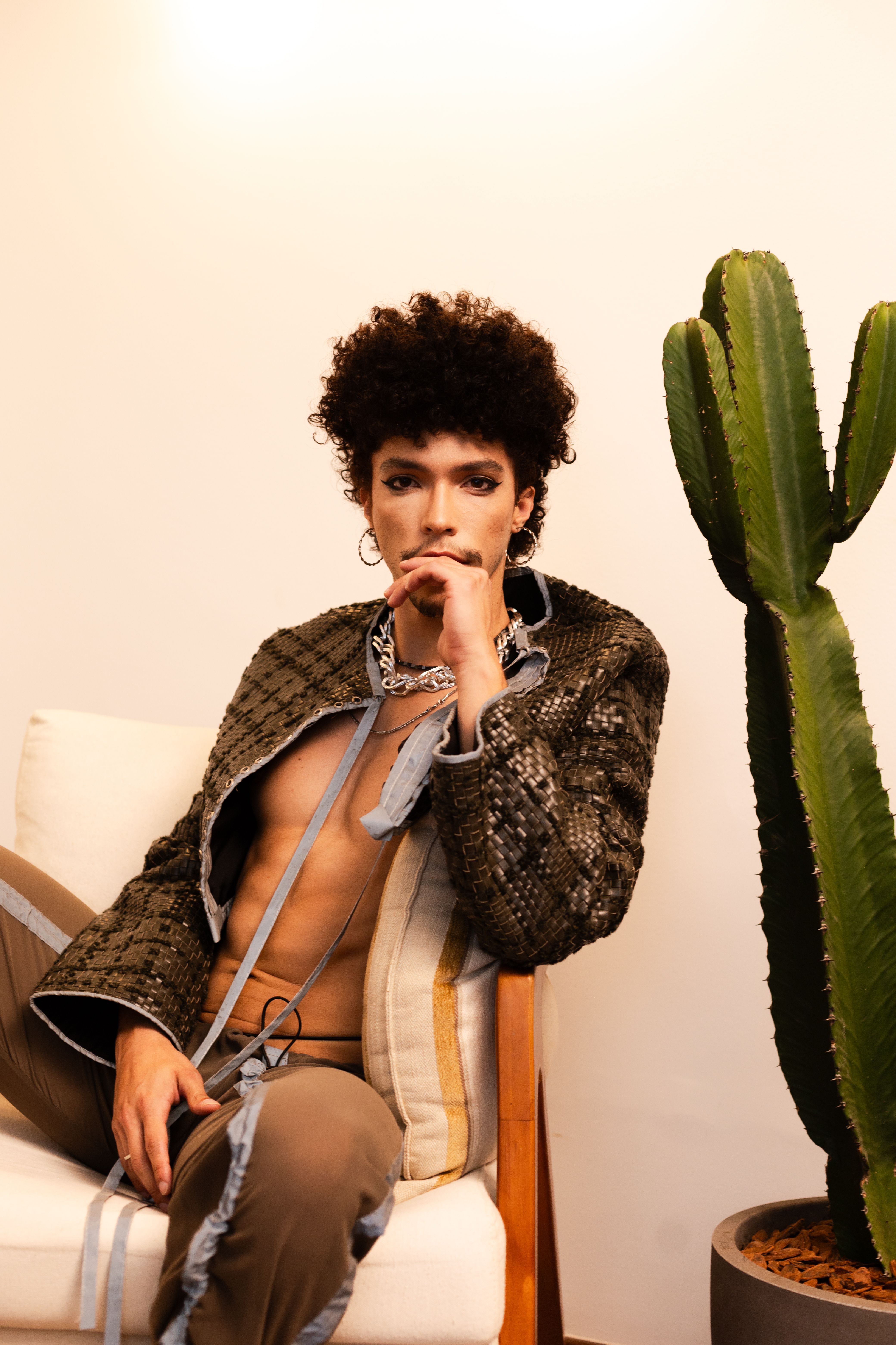 Stylish portrait of a person sitting indoors with a cactus, accentuating modern fashion and design.