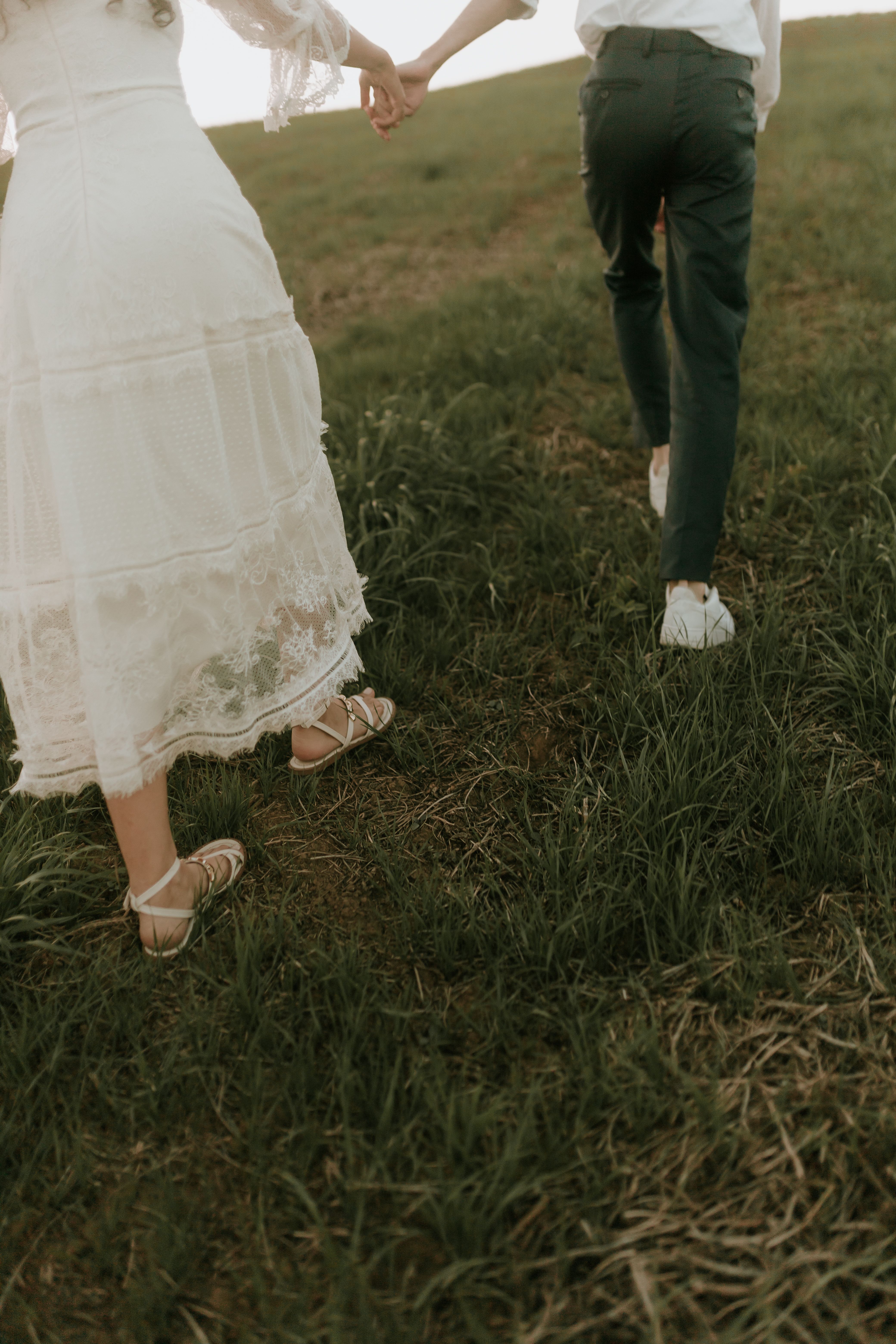Romantic scene of a couple holding hands and walking uphill in a grassy field.