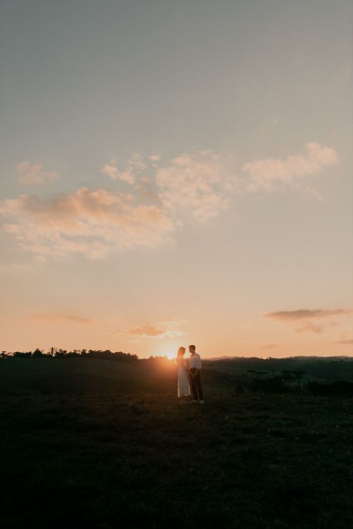 Free A couple shares a tender moment against a beautiful sunset backdrop in a serene landscape. Stock Photo