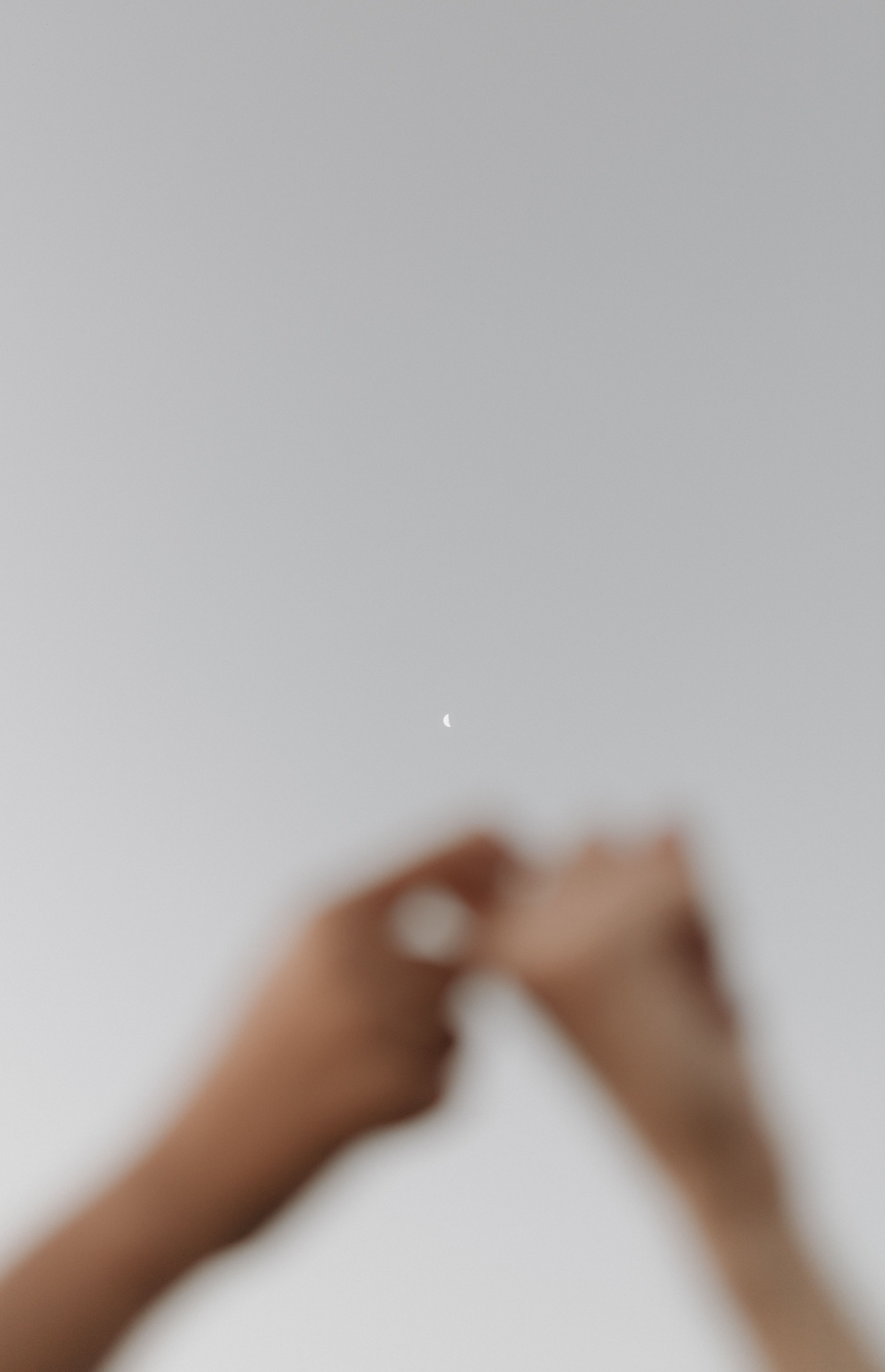 Two hands reaching towards a crescent moon in a minimalist, blurred style.