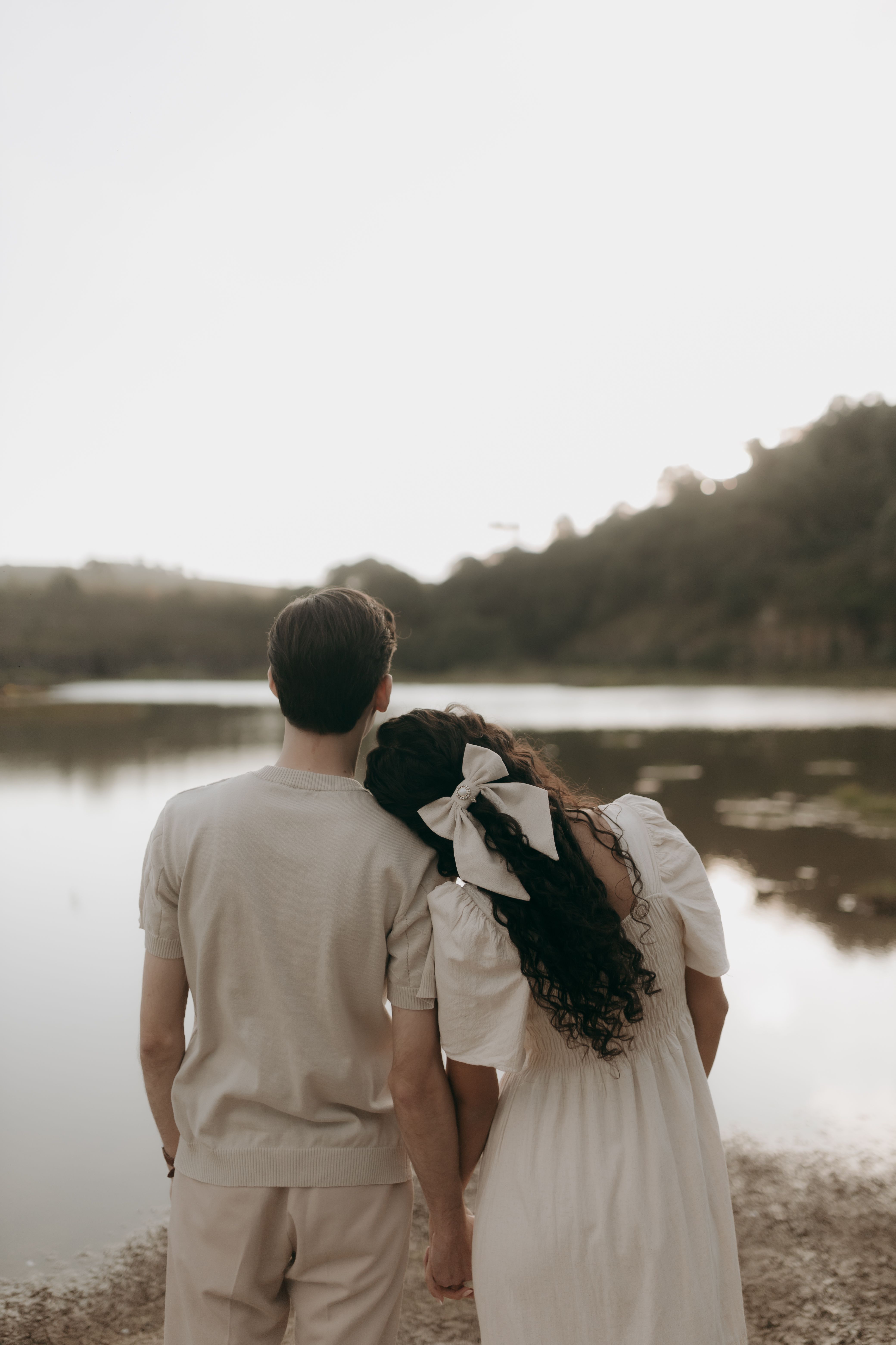 A couple stands together by a serene lake during twilight, embodying romance and tranquility.