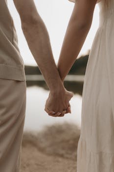 A romantic scene of a couple holding hands near a tranquil waterfront, emphasizing connection and love.