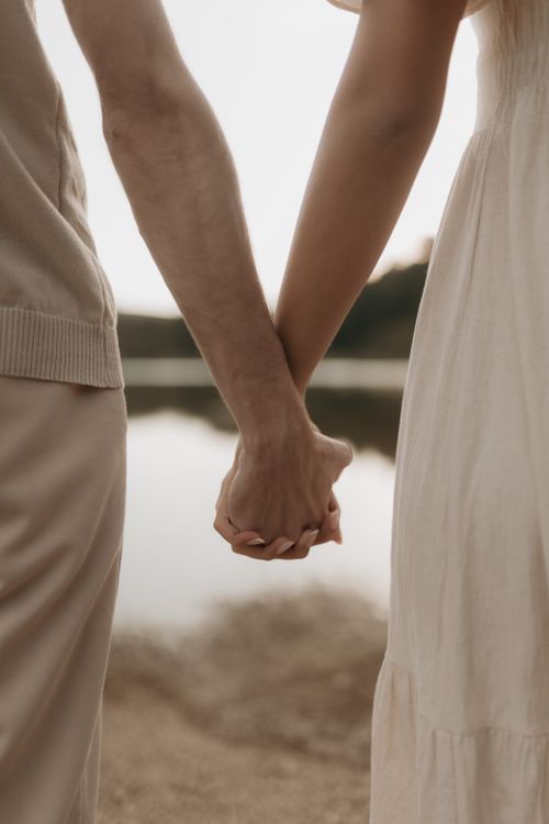 Free A romantic scene of a couple holding hands near a tranquil waterfront, emphasizing connection and love. Stock Photo