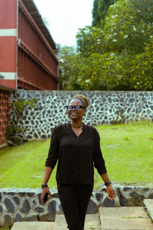 Free A woman in glasses walks confidently in an outdoor setting with greenery and structures. Stock Photo