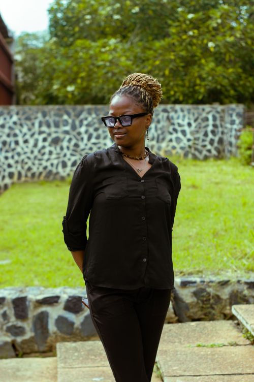 Free Elegant woman in sunglasses poses confidently in outdoor setting with stone and greenery. Stock Photo