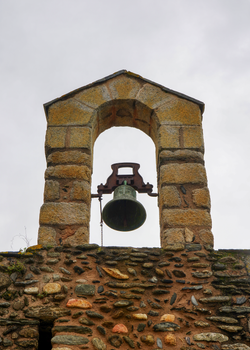 A vintage stone bell tower with a weathered appearance set against a cloudy backdrop.