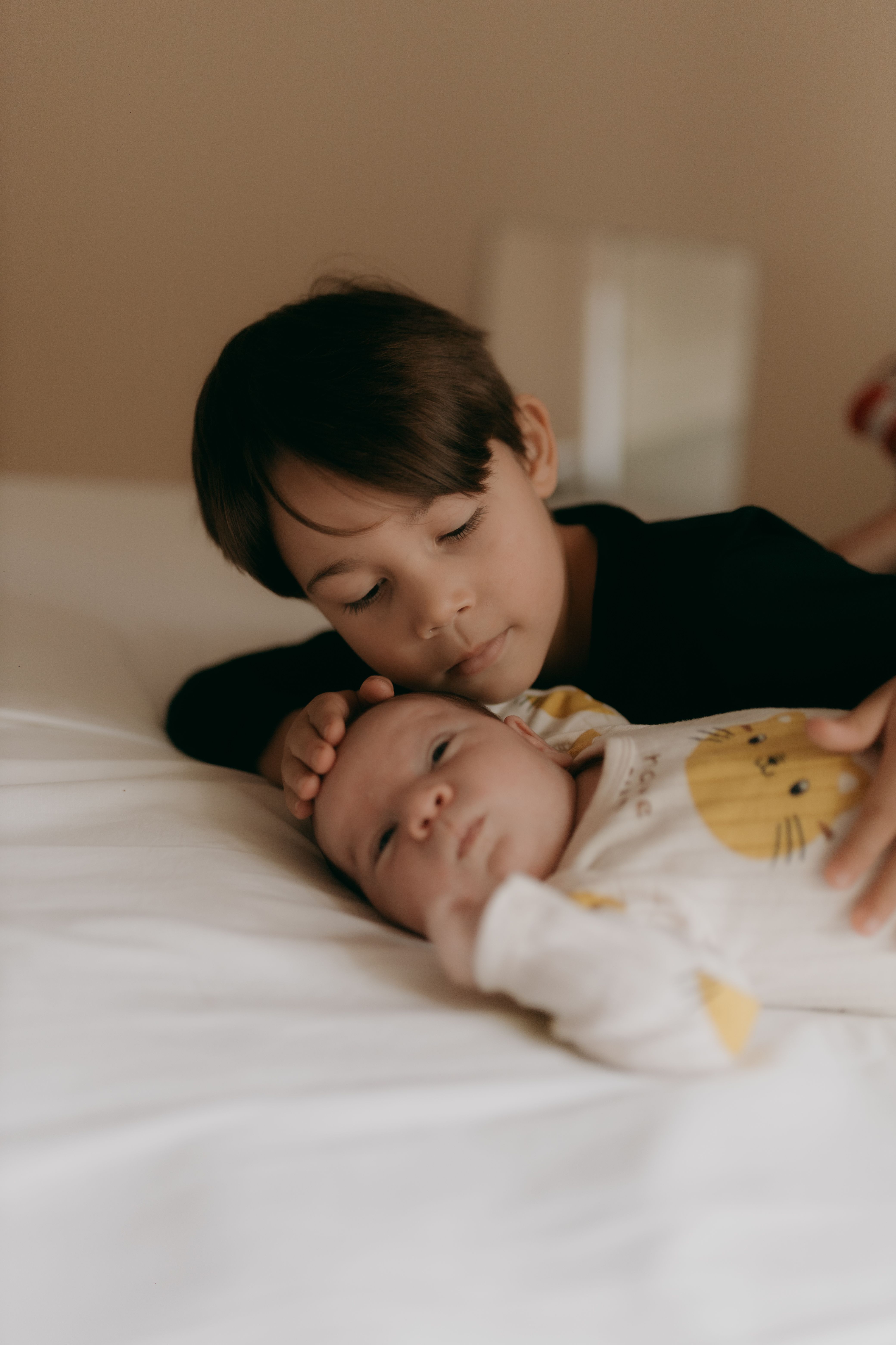 A heartwarming scene of a young boy gently caring for his baby sibling indoors.