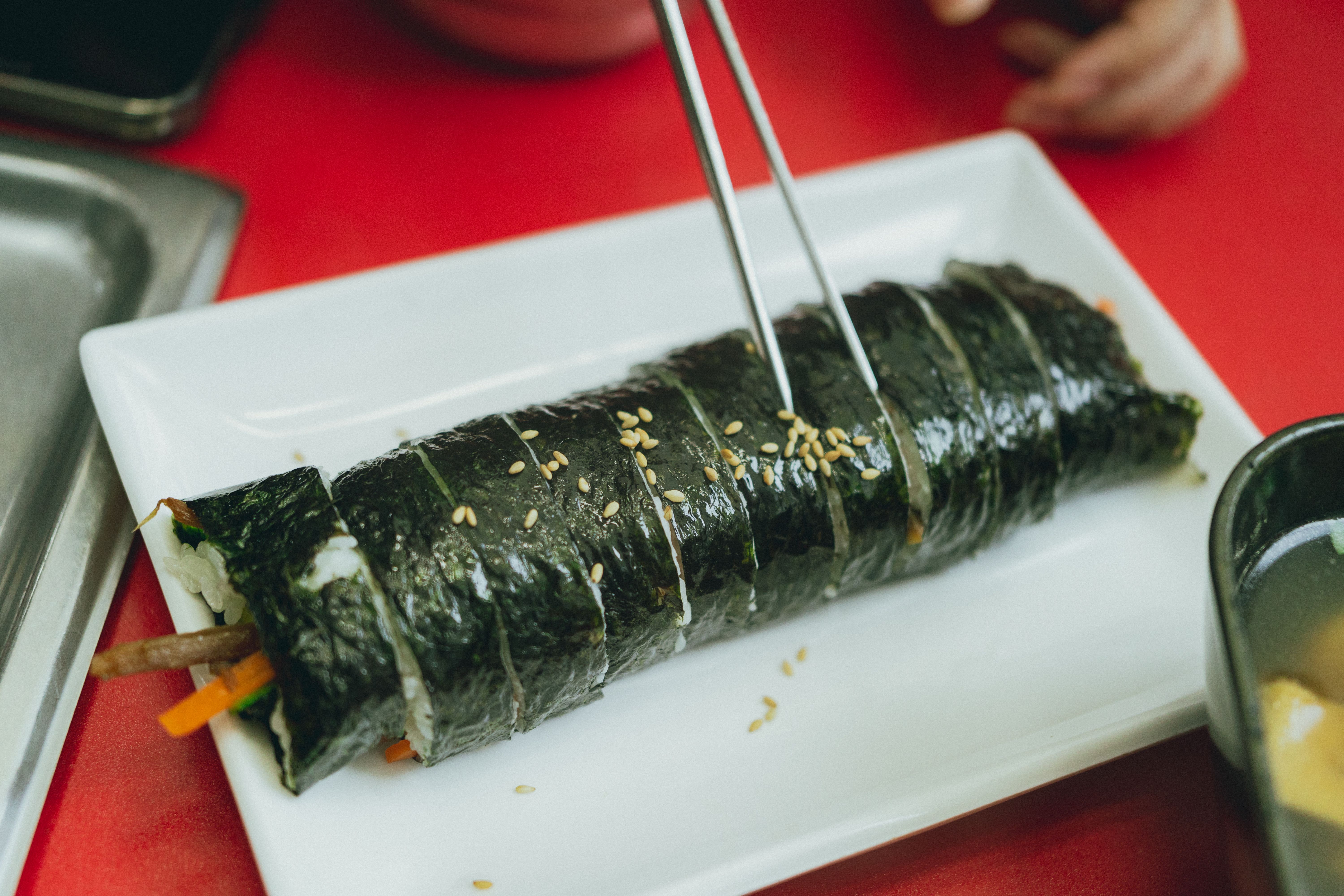 Delicious Korean kimbap served on a white plate with vibrant red background, perfect for culinary exploration.