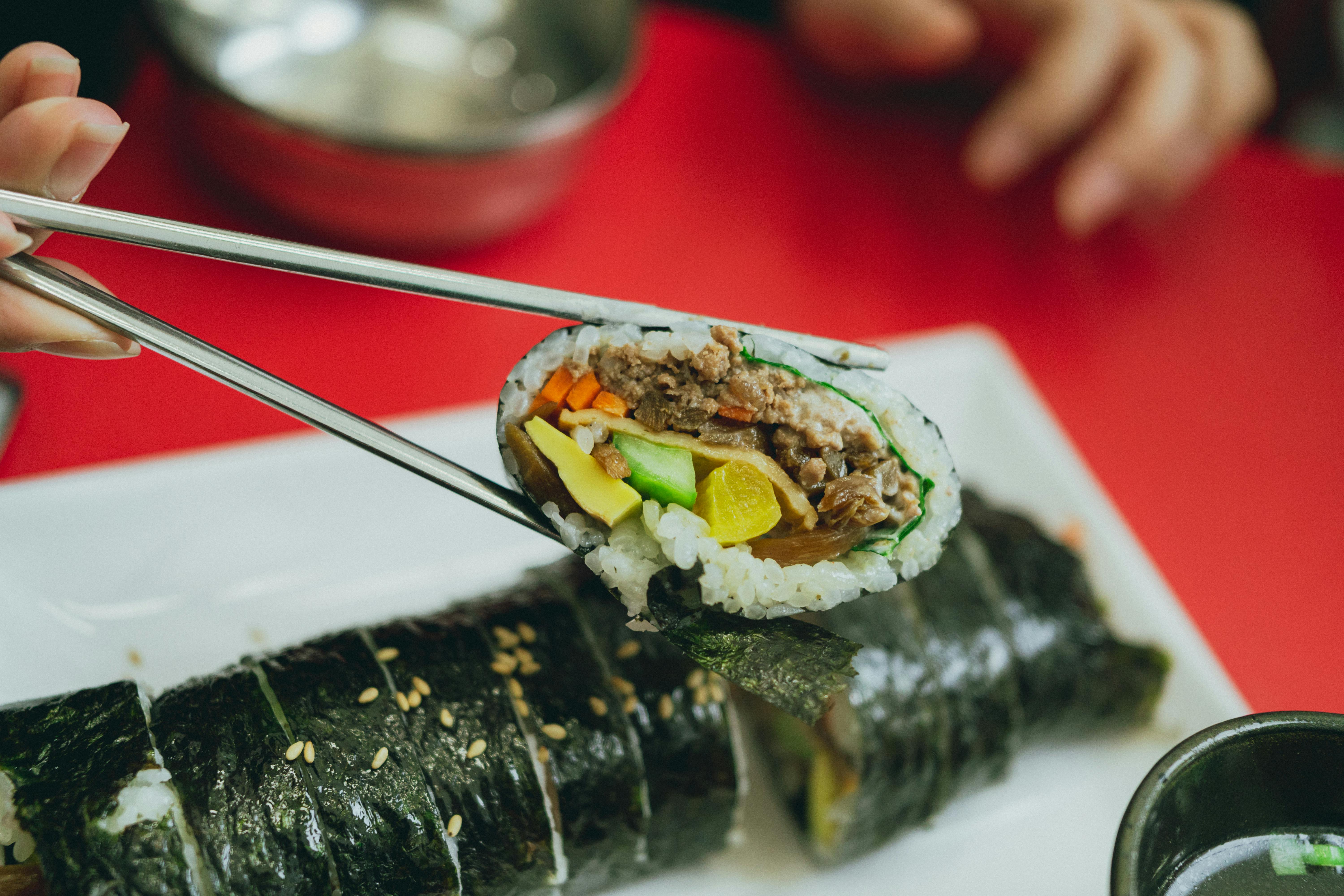 A close-up of a tasty Korean gimbap roll held by chopsticks, showcasing fresh ingredients.