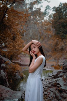 这幅肖像画描绘了一位身穿白色连衣裙的女子，她若有所思地在河岸边摆着姿势，画面十分宁静