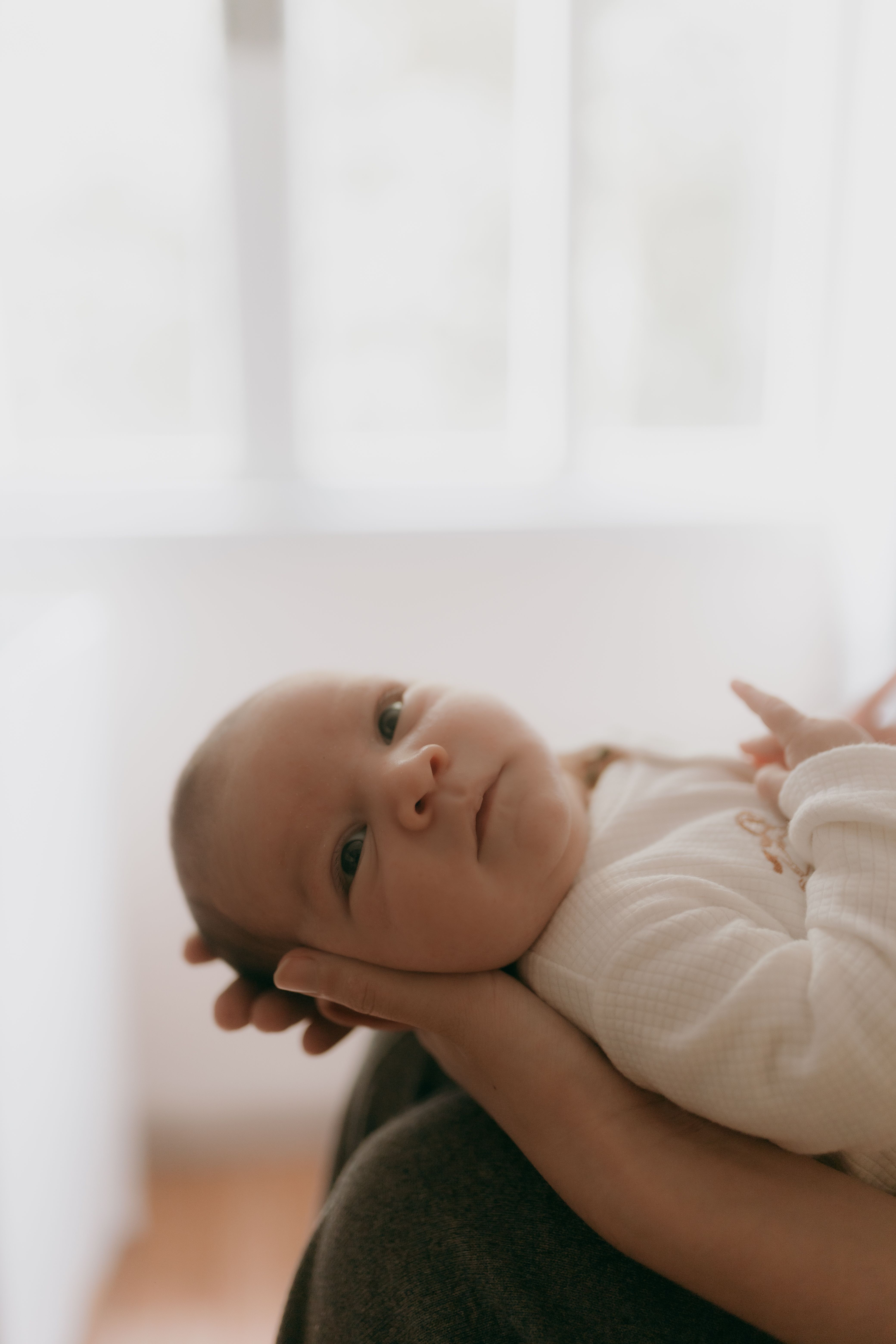 Tender close-up of a newborn baby being gently cradled, captured in soft natural light.