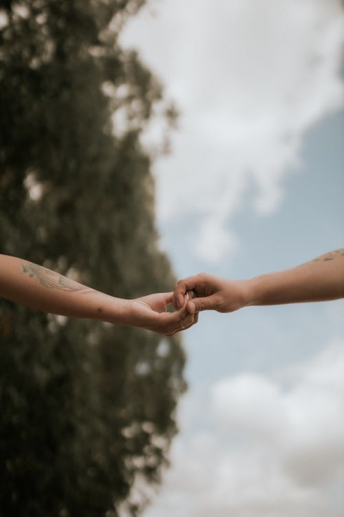 Free A close-up of two hands reaching out amidst a natural outdoor backdrop with blue skies. Stock Photo