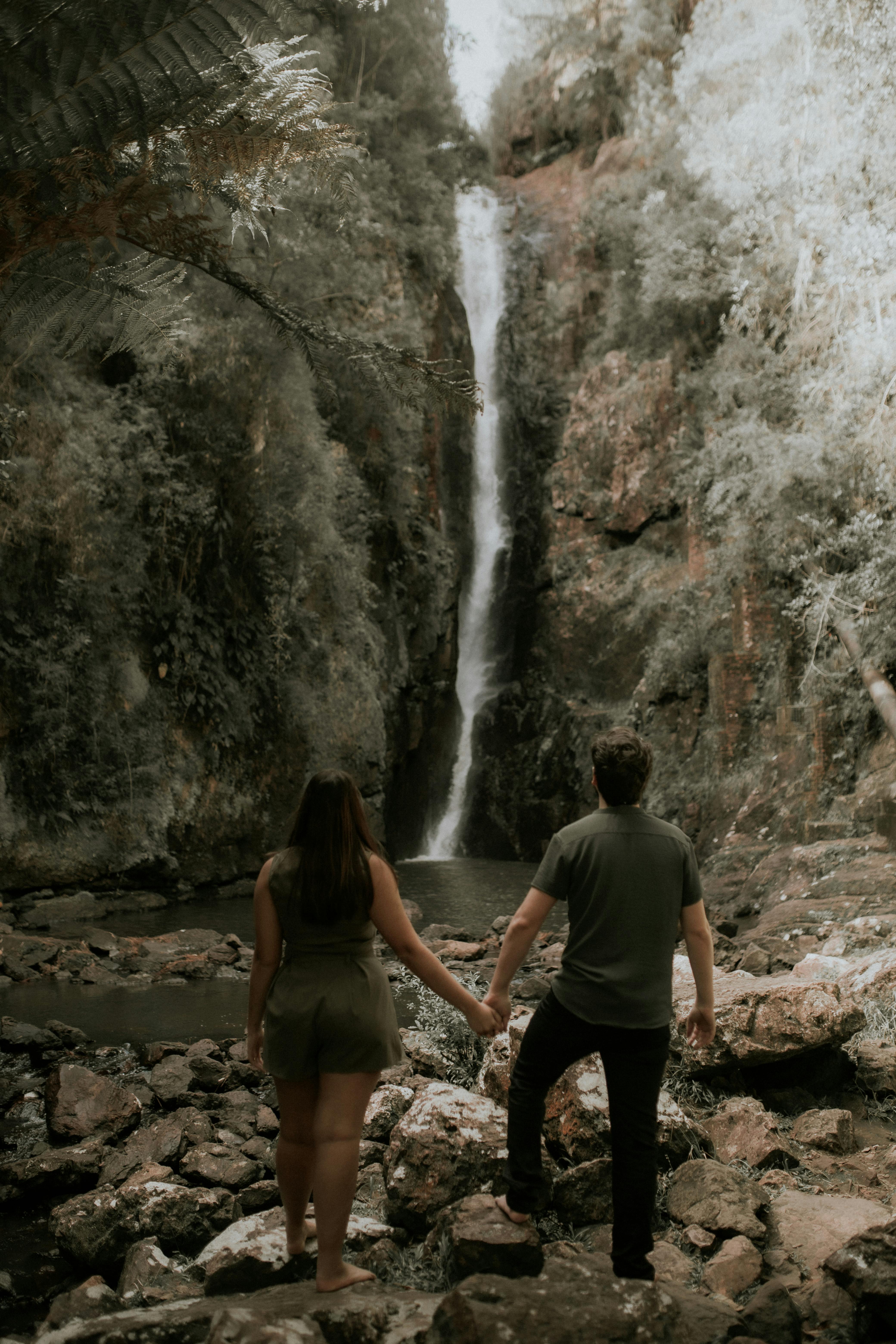 A couple holding hands while admiring a stunning waterfall during a nature hike.