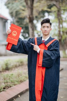 Young adult in graduation gown holding diploma certificate outside for graduation celebration.