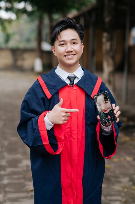 Young graduate in cap and gown celebrating via video call outdoors.