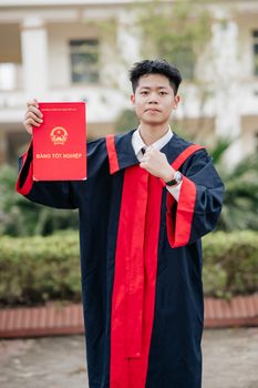 Proud young graduate in gown holding diploma outdoors.