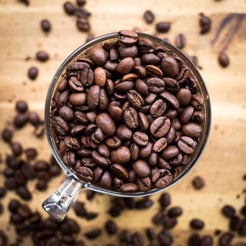 Free High-angle shot of coffee beans in a transparent cup on a wooden surface. Stock Photo