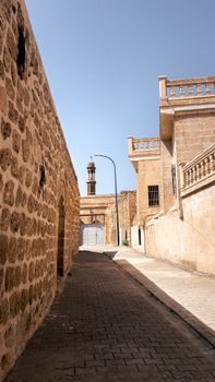 Explore a serene stone alleyway leading to a minaret under a bright blue sky, capturing historic architecture.