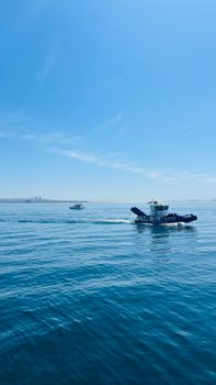 A small fishing boat traverses the tranquil ocean water under a clear, expansive blue sky.
