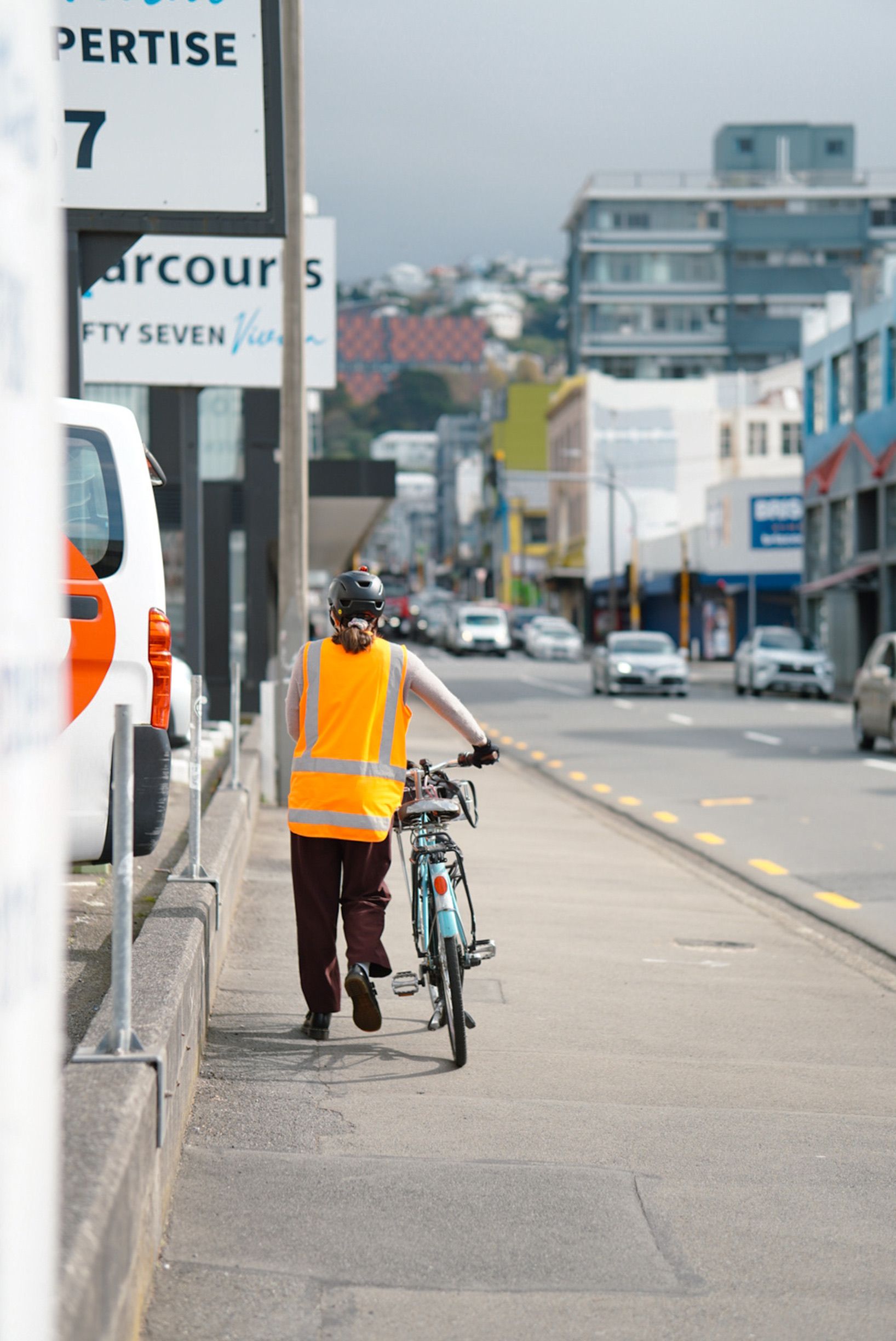 A person in a safety vest walks their bicycle on a city street in Wellington, New Zealand.