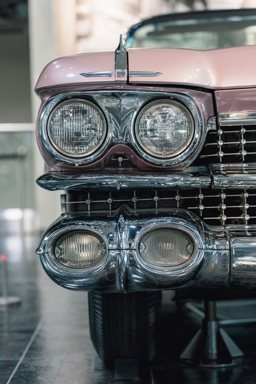 Free Detailed view of a vintage pink car's front headlights and chrome details indoors. Stock Photo