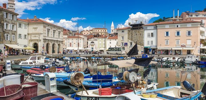 Vibrant harbor in Piran, Slovenia featuring boats and historic architecture under a clear blue sky.