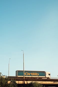 A large truck crosses a bridge under a clear blue sky, suggesting transportation or logistics.