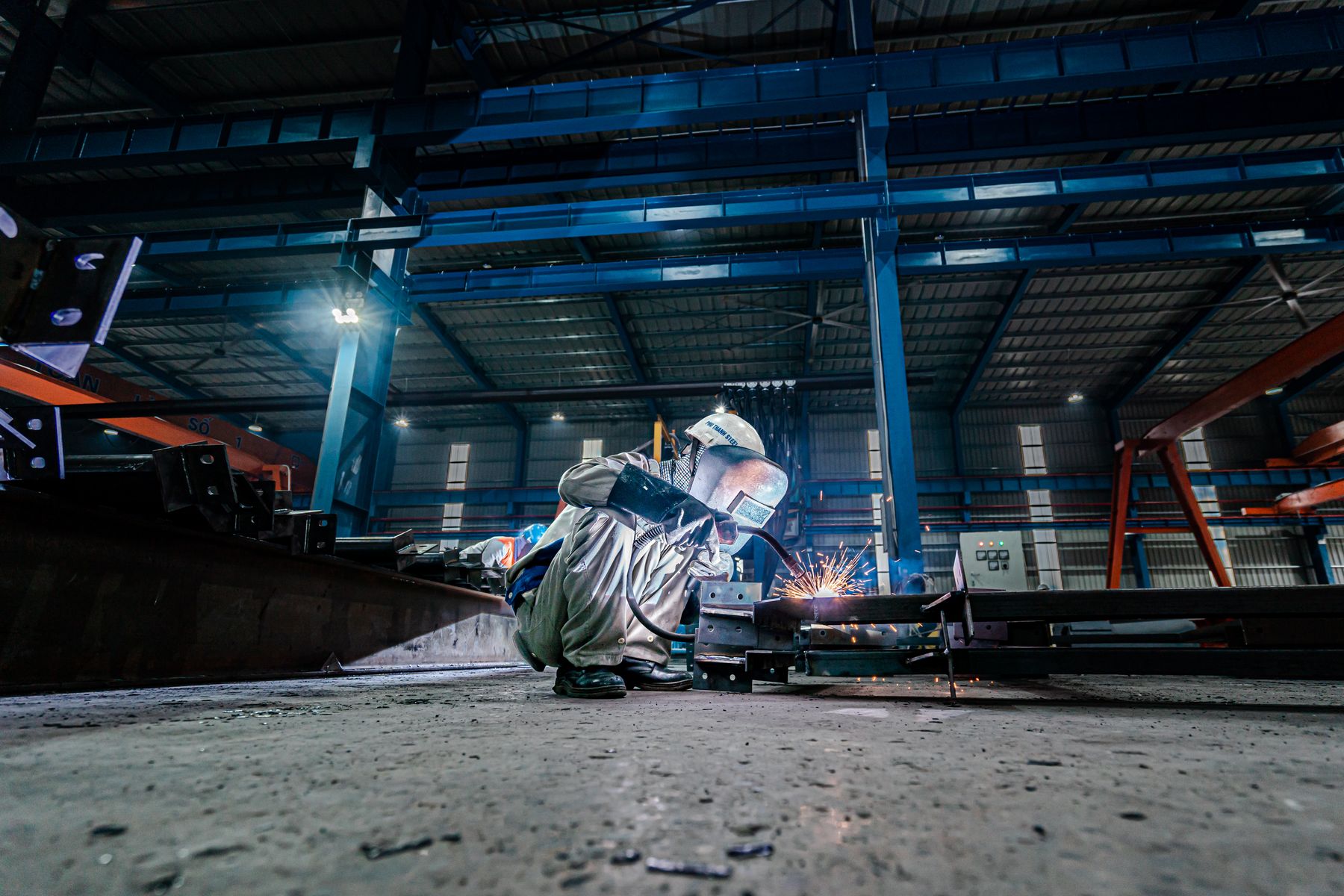 Welder working on a steel structure inside the fabrication shop, sparks lighting the bay